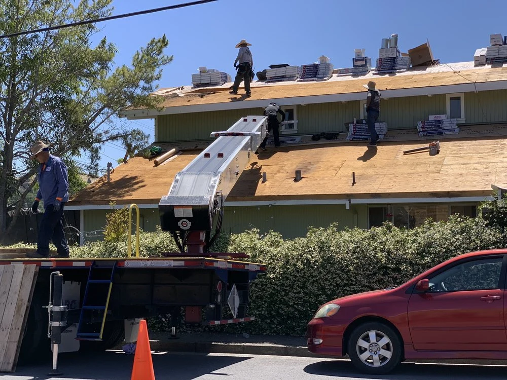 Residential reroofing work with exposed roof decking and material delivery equipment