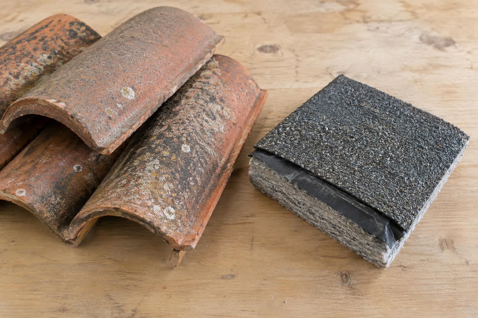 Clay roof tiles beside a layered underlayment sample on a workbench